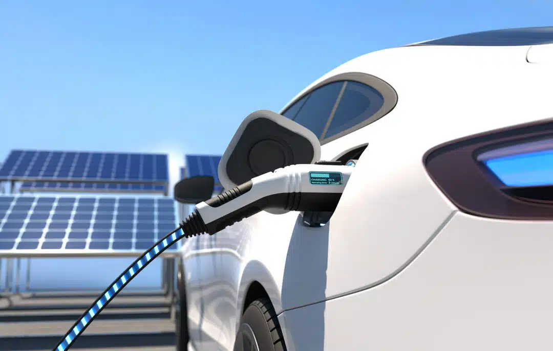 White electric car charging in front of solar panels.